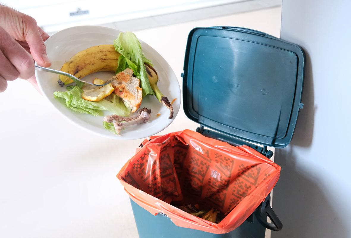 Gros plan sur des mains vidant une assiette de déchets de cuisine dans un sac orange
