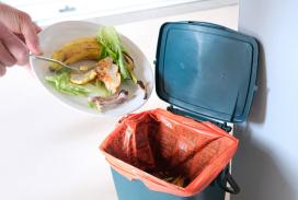 Gros plan sur des mains vidant une assiette de déchets de cuisine dans un sac orange